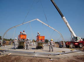 Inmates wearing hard hats help at the construction site by erecting the first frame of the tent.